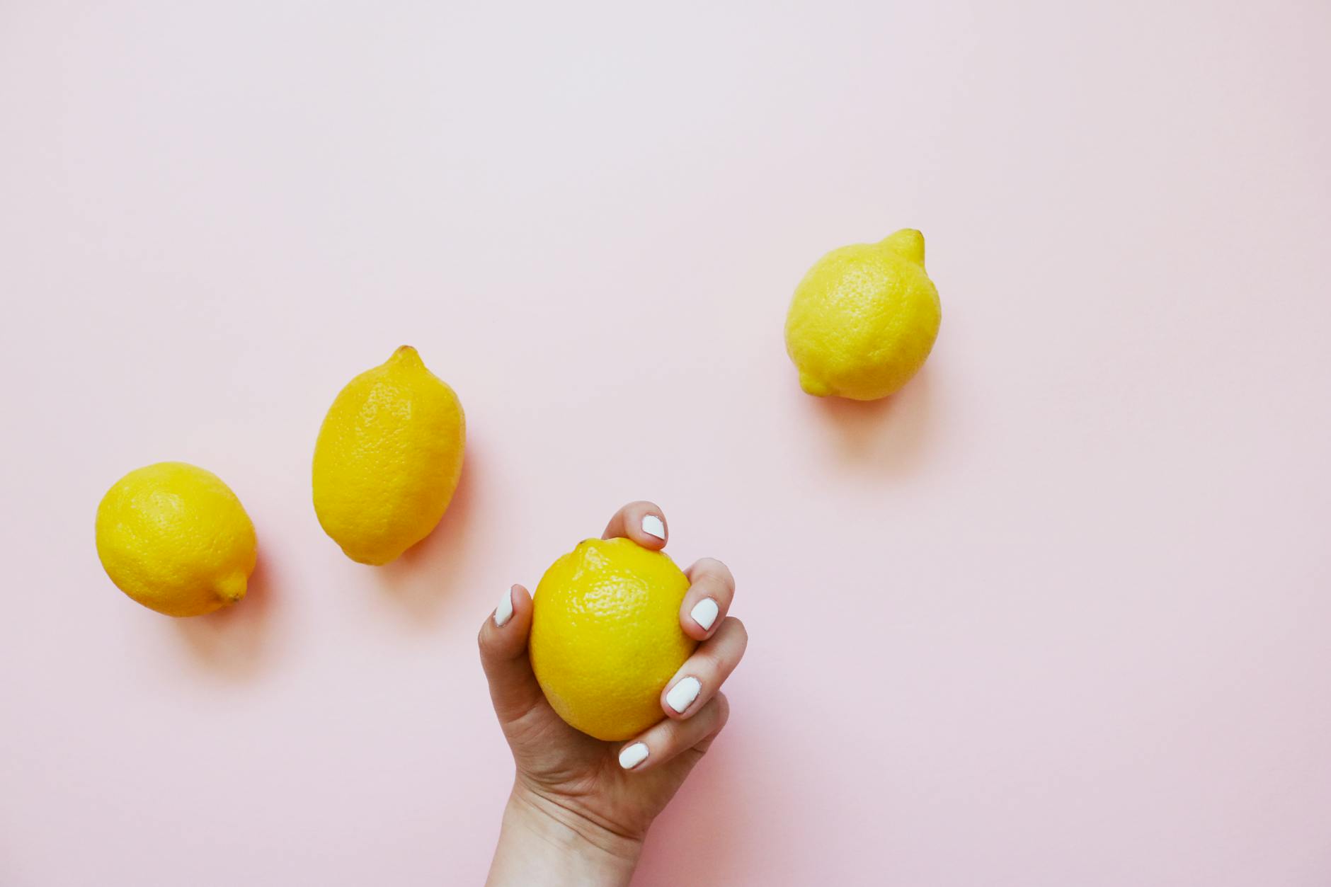 Une main tenant un citron frais sur un fond rose pastel, symbolisant la fraîcheur et la sensualité
