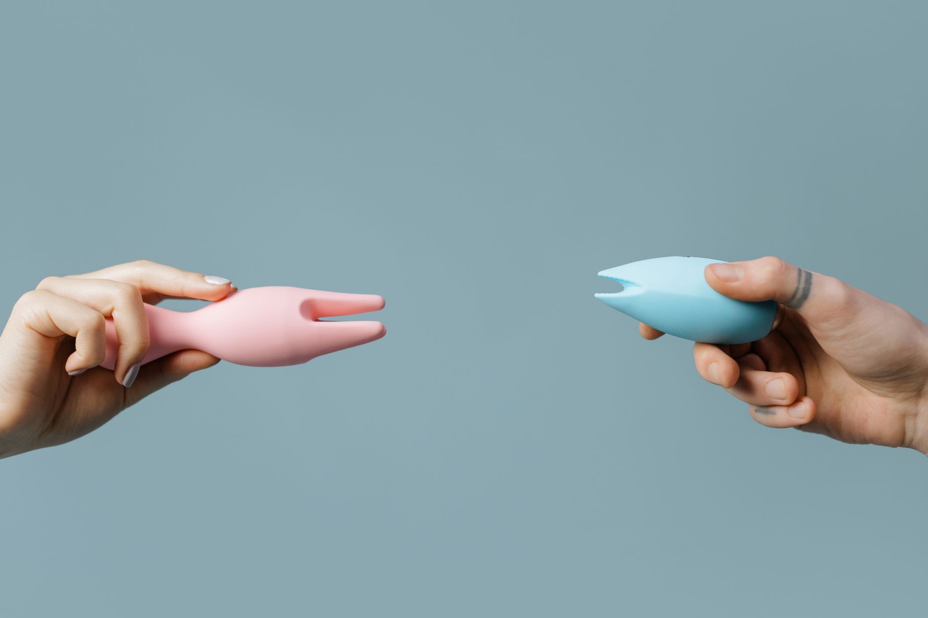 Un vibrateur rose et bleu tenu par deux mains contre un fond pastel, symbolisant l'exploration du plaisir