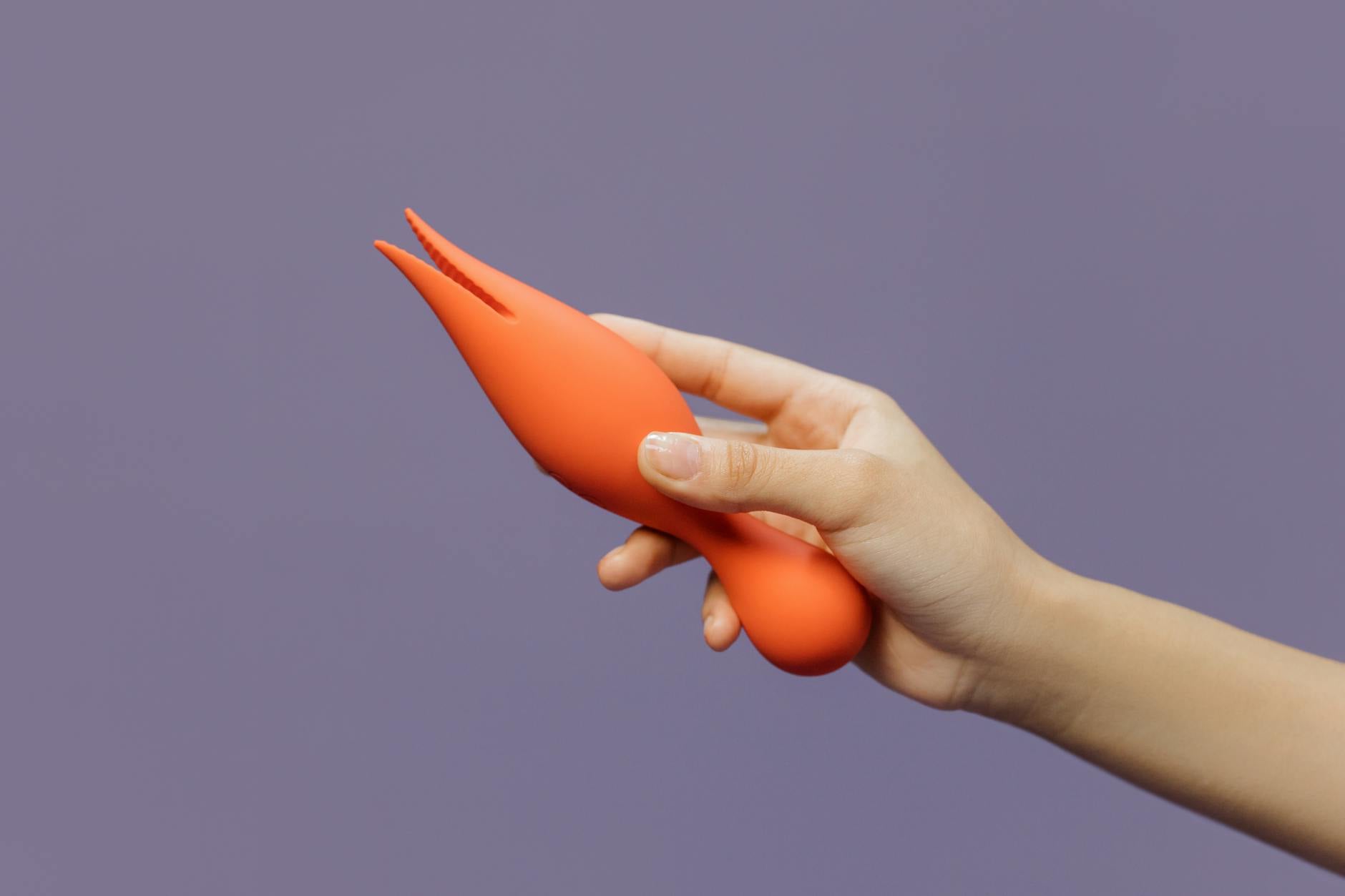 Gros plan d'une main tenant un vibrateur citron contre un arrière-plan violet minimaliste, incarnant la sensualité moderne