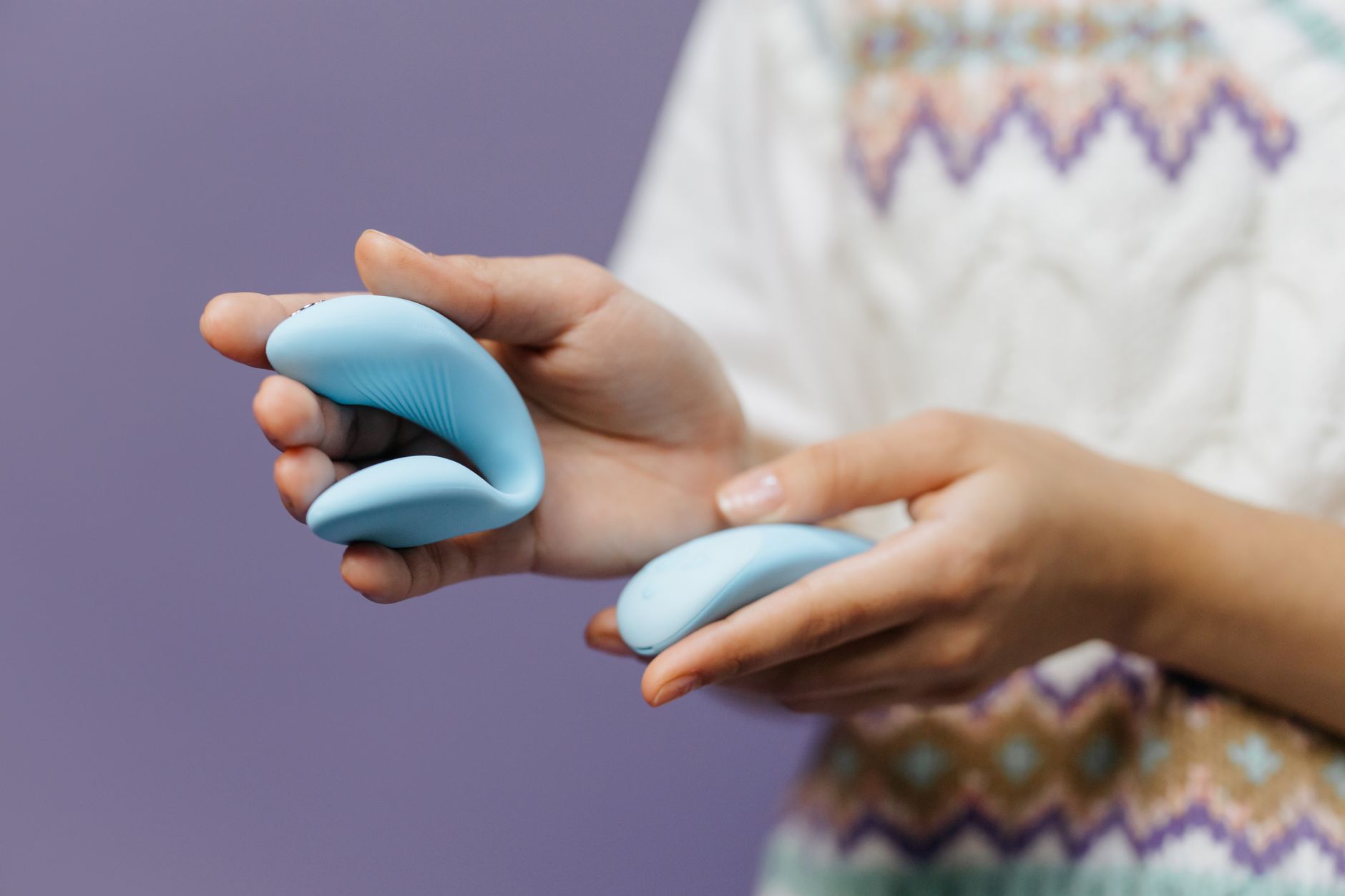 Close-up of hands holding a sleek blue lemon clitoral vibrator against a purple background, symbolizing gentle exploration and reconnection.