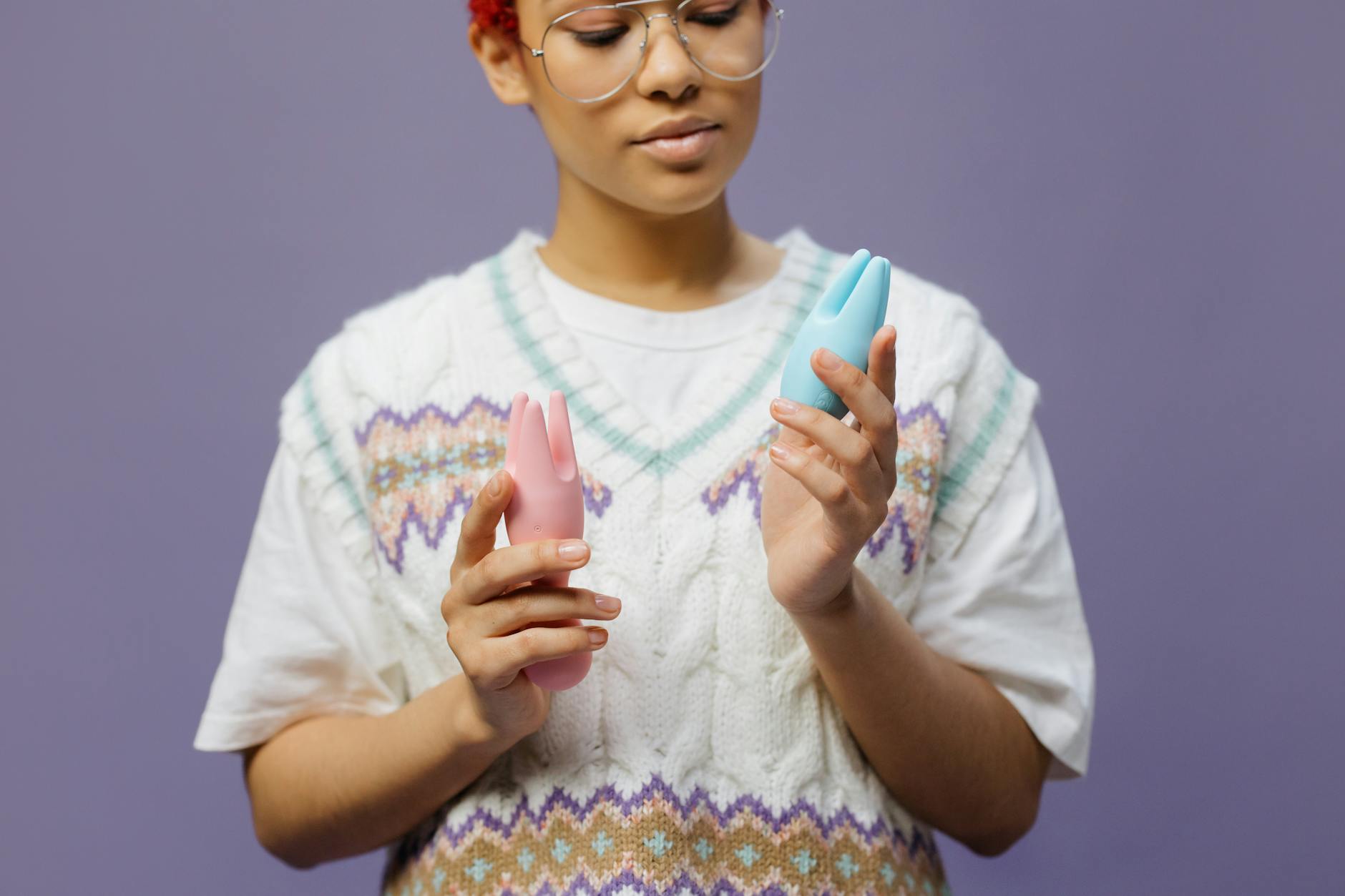 Woman holding blue and pink silicone vibrators in a thoughtful moment during recovery.